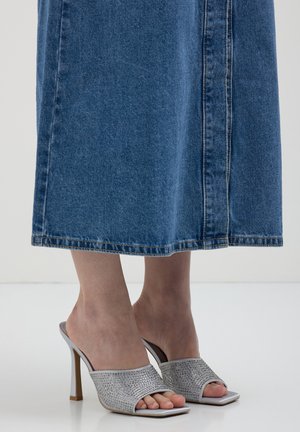 Mule argentate con tacco a zeppa e embellimenti di strass, design aperto sulla punta, tomaia liscia e suola beige, abbinate a una gonna di denim.
