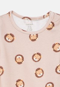 Világos bézs rövid ujjú ing kerek nyakkivágással, barna és gesztenyebarna színű ismétlődő oroszlánfej mintákkal, sima, puha textúrával.