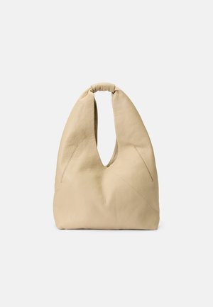 Beige leather shoulder bag with a unique cutout design, soft texture, and a knotted handle; features angled seams for added detail.