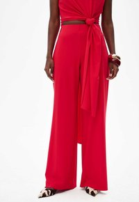 Red wide-leg pants made from a smooth fabric, featuring a tied waist detail. The look is complemented by leopard-print pointed-toe shoes.