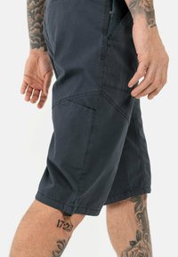 Dunkelblaue Shorts aus atmungsaktivem Stoff, mit seitlichen Taschen, einer strukturierten Oberfläche und einem dekorativen Zugband am Saum.