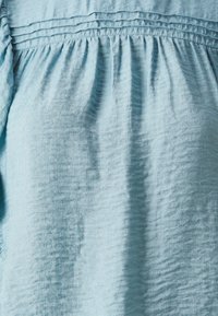 Tessuto azzurro chiaro con una finitura texture, featuring pieghe lungo la parte superiore e un design arricciato, che crea un aspetto fluido.