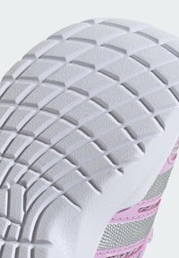 Sole tenisky s tlustým bílým gumovým materiálem, texturovaným povrchem, hlubokým vzorem podrážky a růžovými a stříbrnými akcenty.