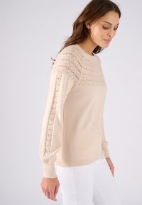 Beige gebreide trui met een delicate kantpatroon op de schouders en mouwen, met lange mouwen en een ronde halslijn.