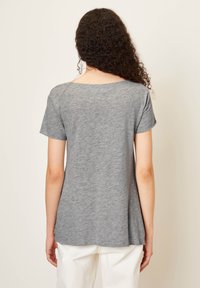 Pilkas trumpas rankovėmis marškinėliai pagaminti iš minkštos medžiagos, su apvalioms iškirptėms ir laisvu siluetu, siaurėjančiu ties apačia, dėvimi su baltais kelnais.