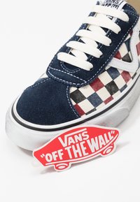 Tummansininen ja ruudullinen Vans-kengät, joissa on valkoiset nauhat, valkoinen pohja ja punainen "Vans Off The Wall" -skeittilogo.