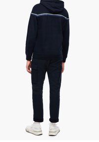 Felpa navy con cappuccio e dettagli a righe sulle spalle, abbinata a pantaloni cargo navy con tasche laterali e orli arrotolati.