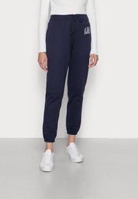 Marina blå joggerbyxor i mjukt tyg, utrustade med elastisk midja med dragsko, muddade vristhål och en logotyp på vänster lår.