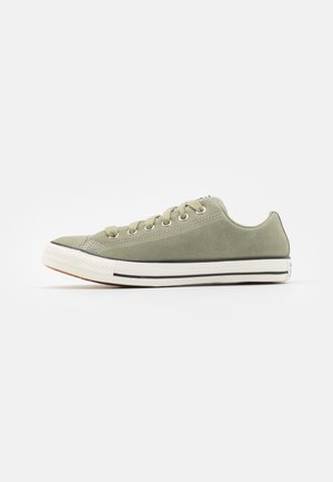 Zapatilla de lona verde con suela de goma blanca, línea de acento negra, ojales de metal y diseño de punta redondeada. Silueta de caña baja.