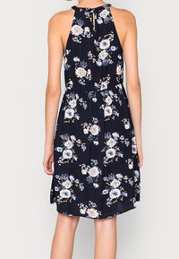 Vestido floral navy con cuello halter, que presenta flores en azul claro y crema, una cintura ajustada y un detalle de abertura en la espalda.