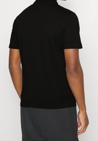 Svart pikétröja med korta ärmar, tillverkad av textil med struktur. Har en klassisk krage och enkel nederkant, tillsammans med grå sportshorts.