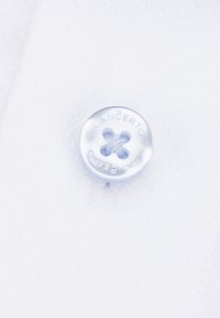 Biała tkanina z jasnoniebieskim guzikiem z wytłoczonym napisem "LANCERTO". Guzik ma cztery otwory, jest gładki i ma delikatny połysk.