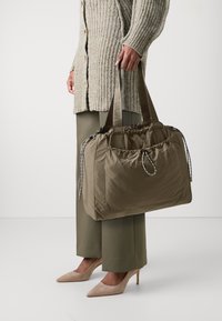 Kaki nylon tote-veske med snøring og sølvhardware, med korte håndtak og strukturert overflate.