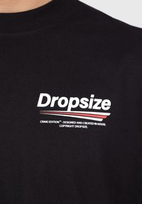 Black cotton t-shirt featuring the word "Dropsize" in bold white letters, accented with red stripes, and a small text below.