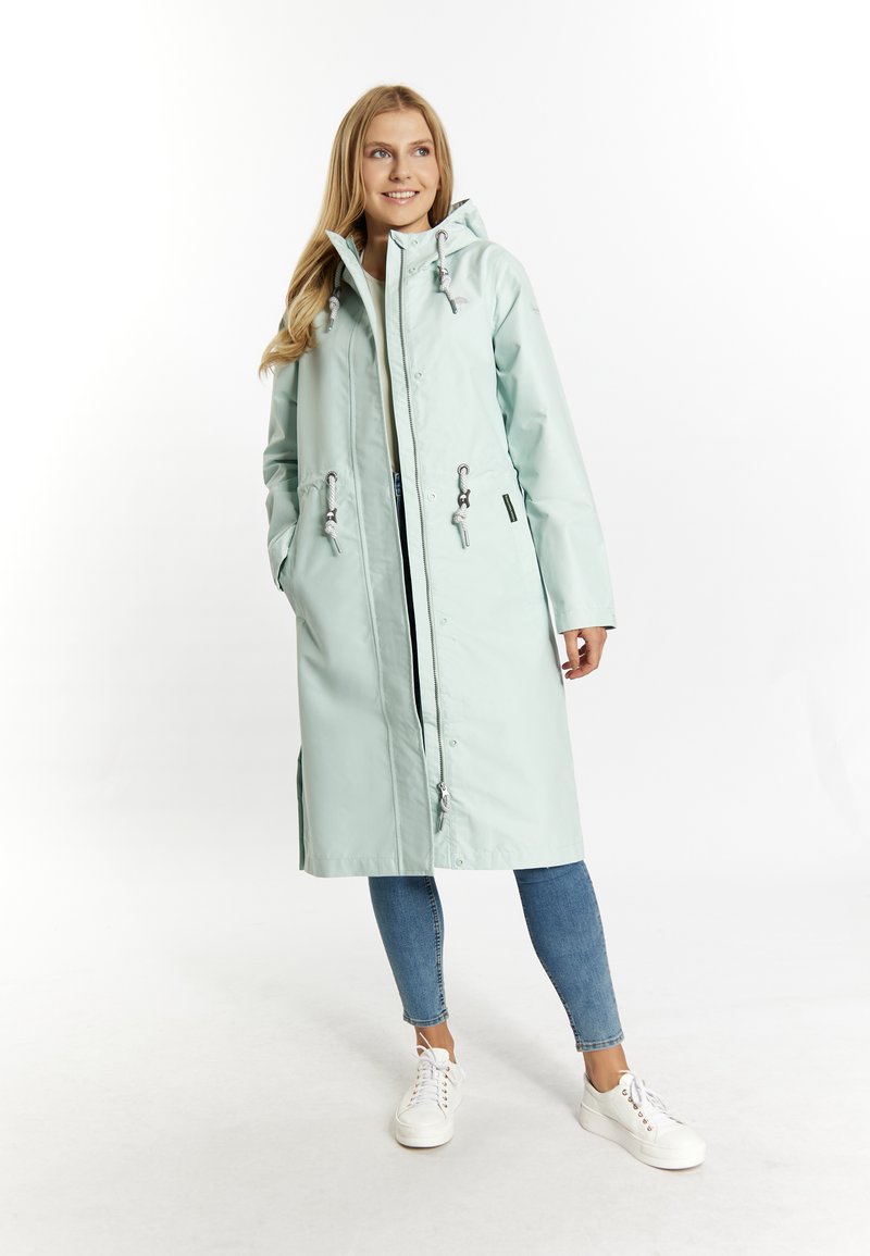 Light mint green waterproof coat with a hood, front zipper, drawstring waist, and side pockets, paired with blue jeans and white sneakers.