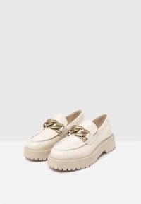 White leather loafers with a chunky beige sole and a gold chain accent on the front. Smooth texture, rounded toe, and low heel.