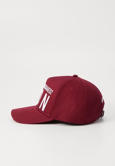 Casquette de baseball bordeaux avec une visière courbée, comportant un texte blanc au-dessus de la visière et sur le côté. Fabriquée en tissu doux avec des détails cousus.