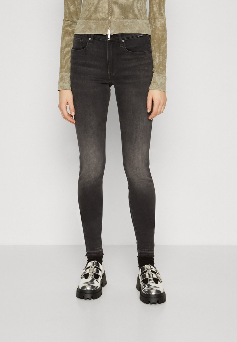 Vaqueros negros ajustados con un acabado desgastado. Llevados con una blusa verde texturizada y zapatos de plataforma plateados, con detalles de hebilla.