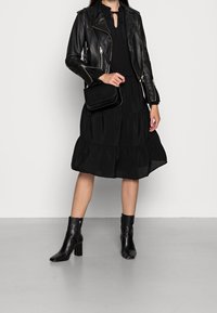 Svart läderbikerskinnjacka över en svart klänning med volangkant, i kombination med ankelstövlar och en liten svart crossbody-väska.