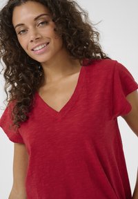 Červený vrchní díl s krátkým rukávem a výstřihem do V vyrobený z texturované tkaniny. Má pohodlný střih s jemnými barevnými variacemi a měkkým splýváním.