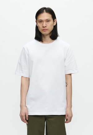 White cotton t-shirt with short sleeves, a crew neck, and a relaxed fit, paired with olive-green pants. No visible logos or patterns.