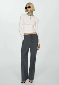 Vit långärmad topp med grön krage och dragkedja, kombinerad med grå rutig vida byxor, som har dragsko i midjan och platt fram.