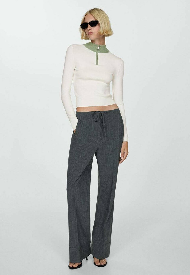 Vit långärmad topp med grön krage och dragkedja, kombinerad med grå rutig vida byxor, som har dragsko i midjan och platt fram.