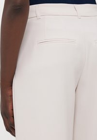 Lichtbeige broek met een gladde textuur, klassieke snit en dubbele achterzakken met zichtbare stiksels.
