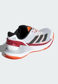 Witte sportschoen met zwarte strepen, rode accenten en een oranje zool. Bovenwerk van mesh met textuurdetails en een gevoerde kraag.