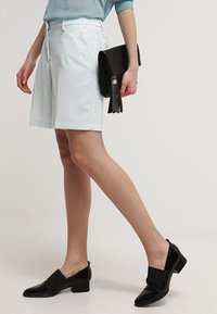 Ljusblå skräddarsydda shorts i mjukt tyg, kombinerade med en svart kuvertväska med tofsdetaljer och svarta lackskor.