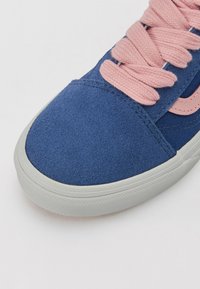 Sneaker bleu en daim avec des lacets roses clairs, bout rond et dessus texturé. Doté d'une semelle en caoutchouc blanche avec un motif de traction.