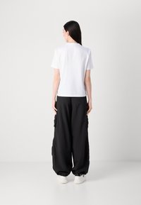 Witte short-sleeve shirt gecombineerd met zwarte cargo-broek met grote zijzakken, losse pasvorm en elastische manchetten. Accessoires zijn onder andere grote oorbellen.
