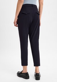 Navyblauwe tapered broeken gemaakt van een gladde stof, met twee achterzakken met kleppen en knoopsluitingen, en een verkorte lengte.