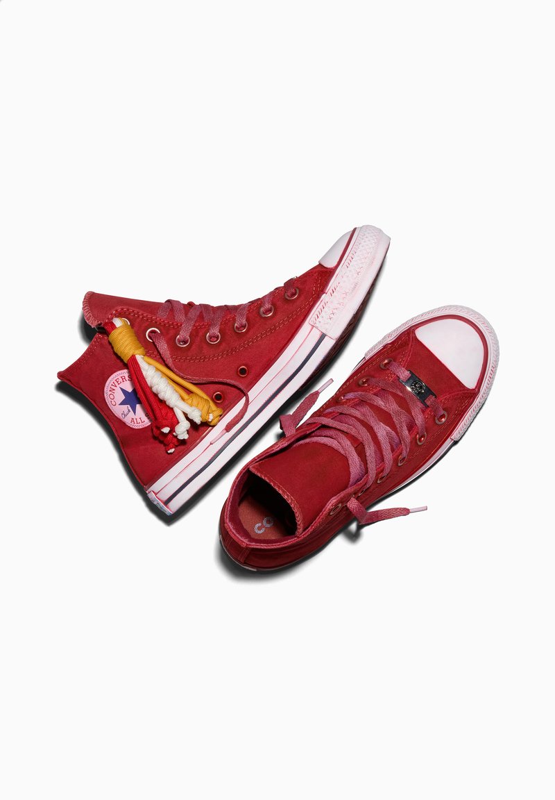 Pair of red high-top Converse sneakers with white rubber toes, pink laces, and decorative yellow and white tassels on one shoe.