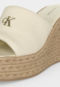 Sandale compensée beige Calvin Klein avec semelle plateforme en corde tressée et logo CK doré sur la bride en tissu.