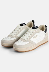 Sneaker bianche e beige realizzate con materiali in camoscio e pelle, punta rotonda, design con lacci, suola in gomma naturale e un accento sul tallone nero.