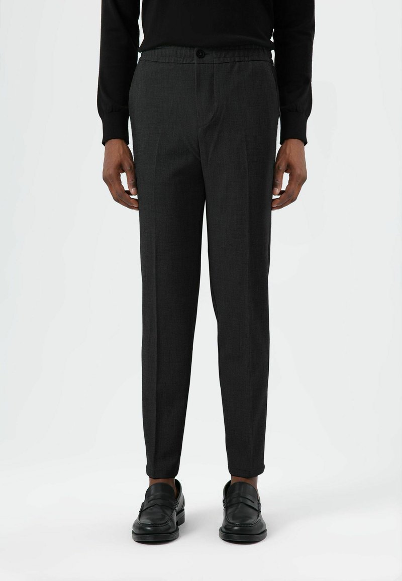 Grijze op maat gemaakte broek met een subtiele textuur, elastische tailleband en een knoop aan de voorkant; gecombineerd met zwarte loafers.