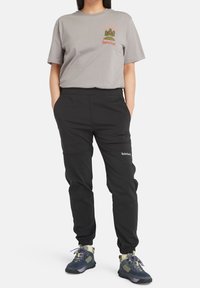 Gray cotton t-shirt with tree graphic and "Timberland" logo, paired with black tapered pants featuring pockets and elastic cuffs.