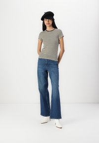 Stripet topp med korte ermer i svart og krem, parret med blå vide jeans. Modellen har på seg en svart beret og hvite hælboots.