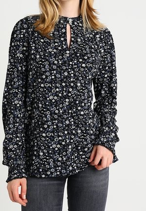 Zwarte blouse met lange mouwen met een kleine witte en blauwe bloemenprint, keyhole halslijn met knoop, gedragen met donkergrijze spijkerbroek.