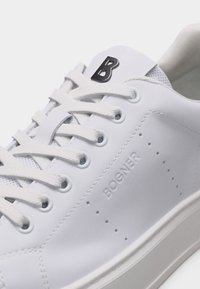 Λευκό δερμάτινο αθλητικό παπούτσι με λευκά κορδόνια, διάτρητες λεπτομέρειες στο πλάι, ανάγλυφη επωνυμία "BOGNER" και μαύρο λογότυπο "B" στη γλώσσα.