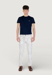 T-shirt blu navy con collo a giro, jeans bianchi e scarpe da barca marroni. Caratteristiche: logo sul petto, silhouette aderente e tessuto liscio.