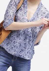 Blouse à motif bleu et blanc avec un col en V, des manches trois quarts et une coupe ample. Portée avec un jean en denim et un sac marron.