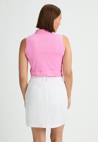 Rosa ärmlös polo-t-shirt i en texturerad tyg, matchad med en vit knälång kjol med två bakfickor och en slät yta.