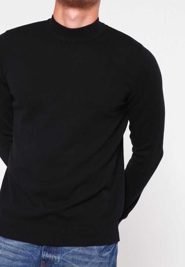 Pull noir à manches longues avec un col montant côtelé. Tissu tricoté avec une texture lisse et coupe ajustée. Porté avec un jean bleu.