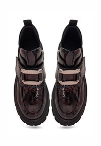 Bottes en cuir verni noir avec une semelle épaisse, dotées d'une large sangle et de boucles métalliques. Texture lisse avec un fini brillant.