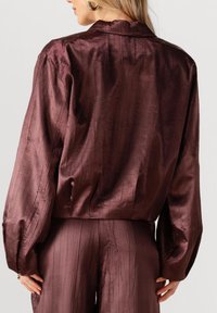 Bordeaux satijnen blouse met een losse pasvorm, voorzien van lange mouwen, subtiele gestructureerde strepen en een kraag.