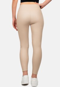Leggings beige realizzati in tessuto elastico, con vita alta e una texture liscia, abbinati a sneakers bianche.