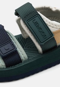 Sandale cu bretele, realizate dintr-un amestec de materiale bleumarin, verde și bej. Talpă texturată și curele ajustabile cu detalii cu logo.
