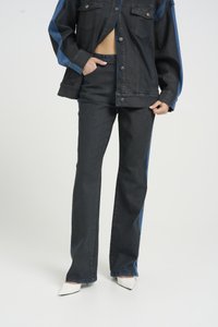 Dark denim jacket with blue accents, paired with matching dark flared jeans. White pointed-toe heels complete the ensemble.